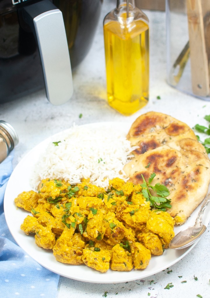 Curry chicken on a white plate with an air fryer in the background. 