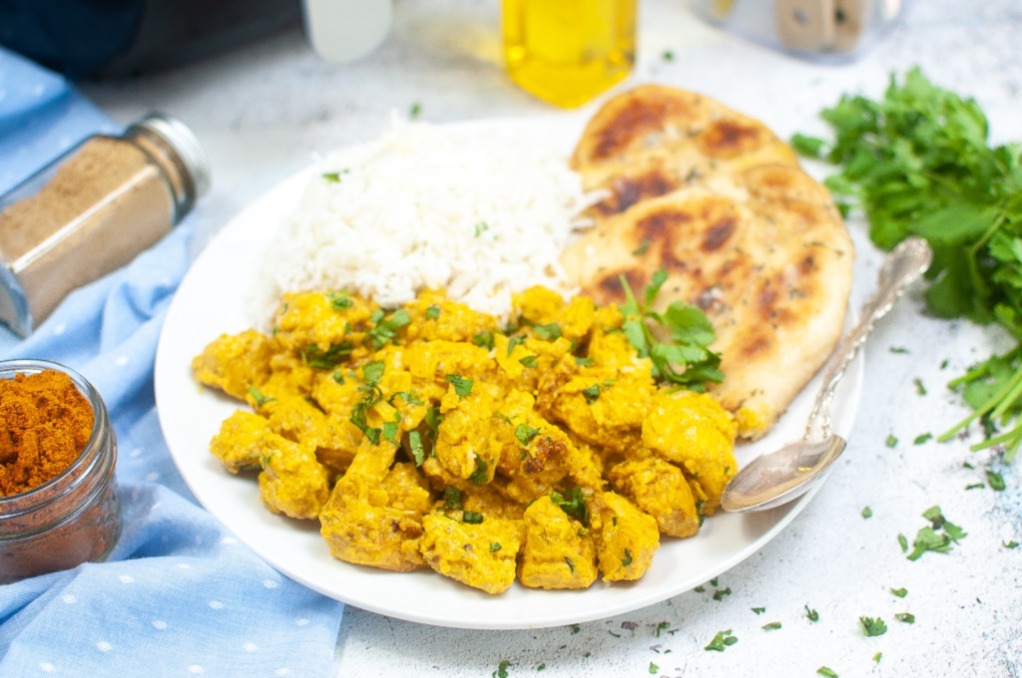 White dinner plate with curry chicken and pita bread on the side ready to eat. 