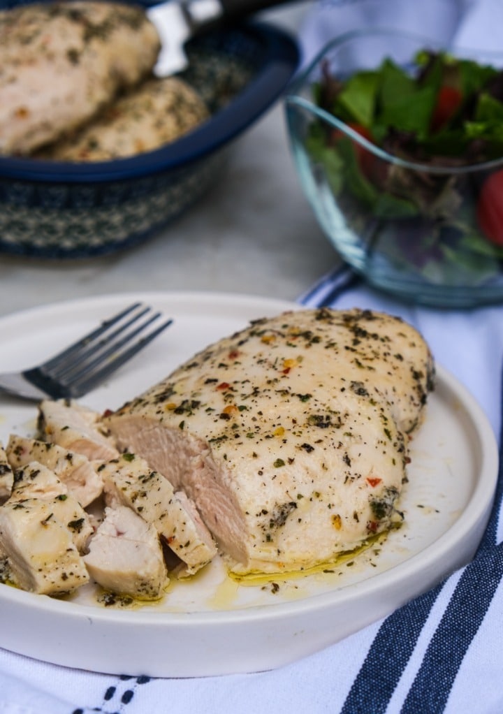 Baked chicken in Italian dressing cooking and on a white dinner plate with salad on the side. 