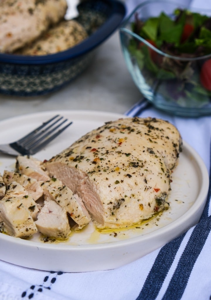 Chicken breast sliced and on a white dinner plate with a fork on the side. 