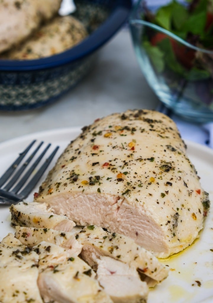 Baked skinless chicken sliced on a white serving dish. 