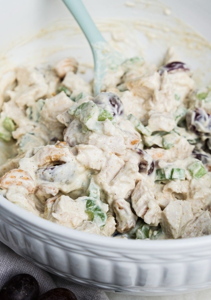 Chicken salad in a white serving bowl with a light blue spoon. 