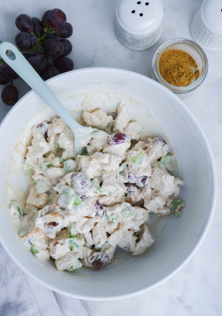 Curried chicken salad in a white serving bowl with curry powder mix on the side. 