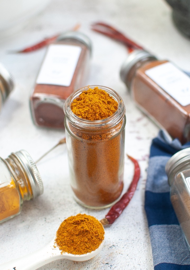 Homemade curry powder seasoning mix in a clear spice jar with spices on the side. 