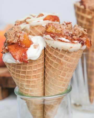 Three sugar cones in a small glass filled with cobbler and cheesecake ready to eat.