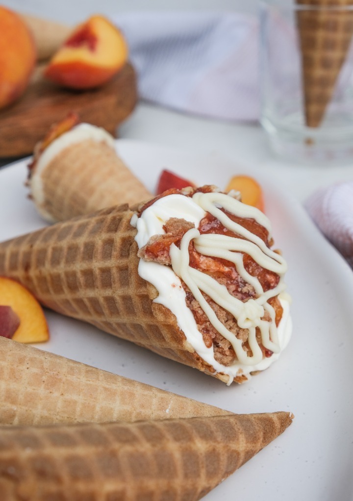 Waffle cones on a white plate with peach cobbler.