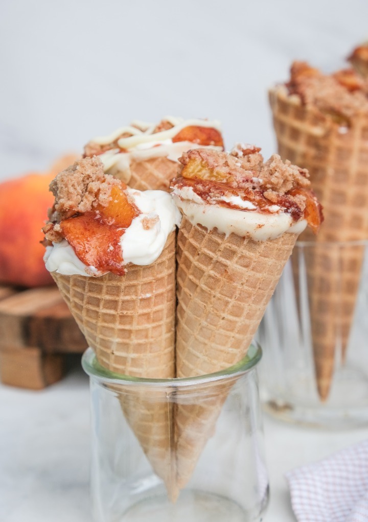 Ice cream cones with peach cobbler in the center ready to eat. 