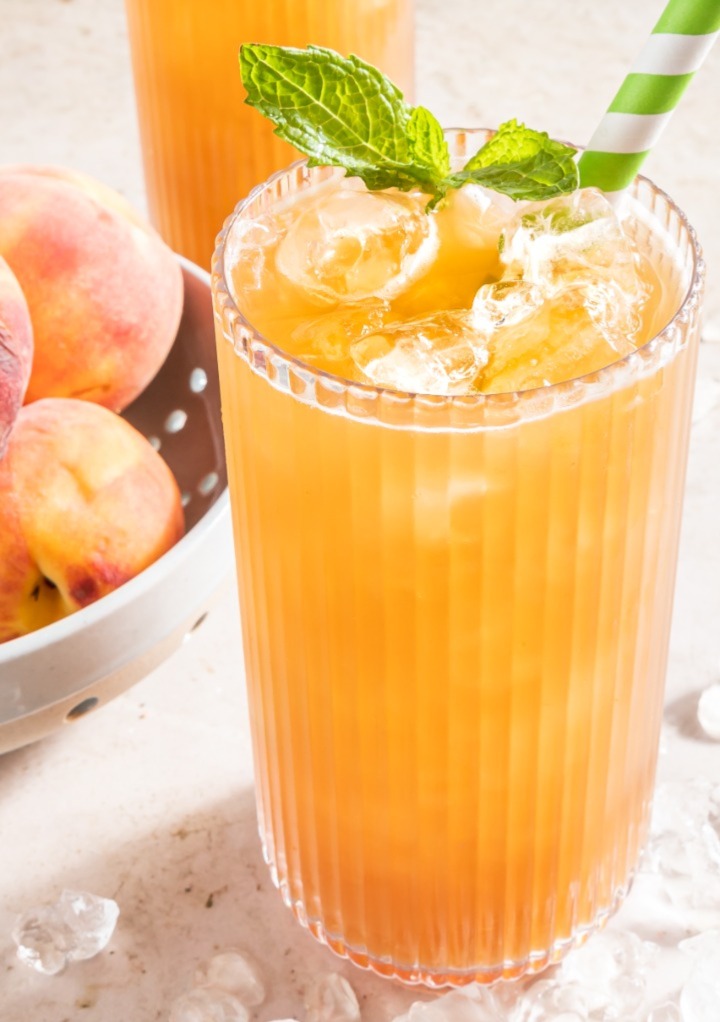 Homemade fresh peach tea in a clear glass with a green and white straw. 