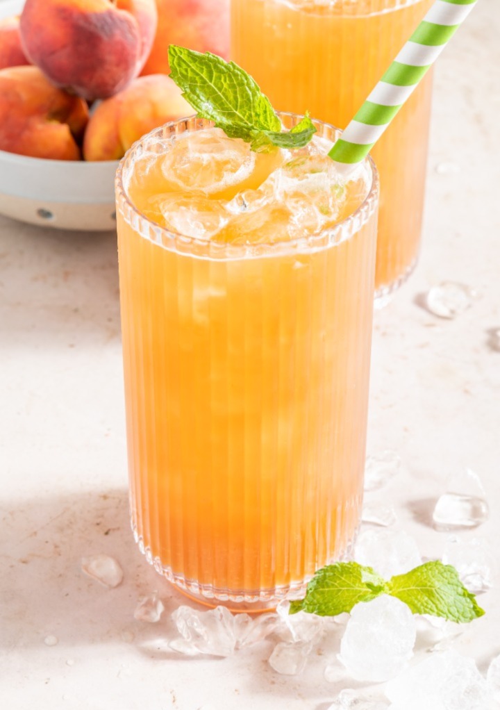 A clear glass of peach tea topped with a mint leaf. 