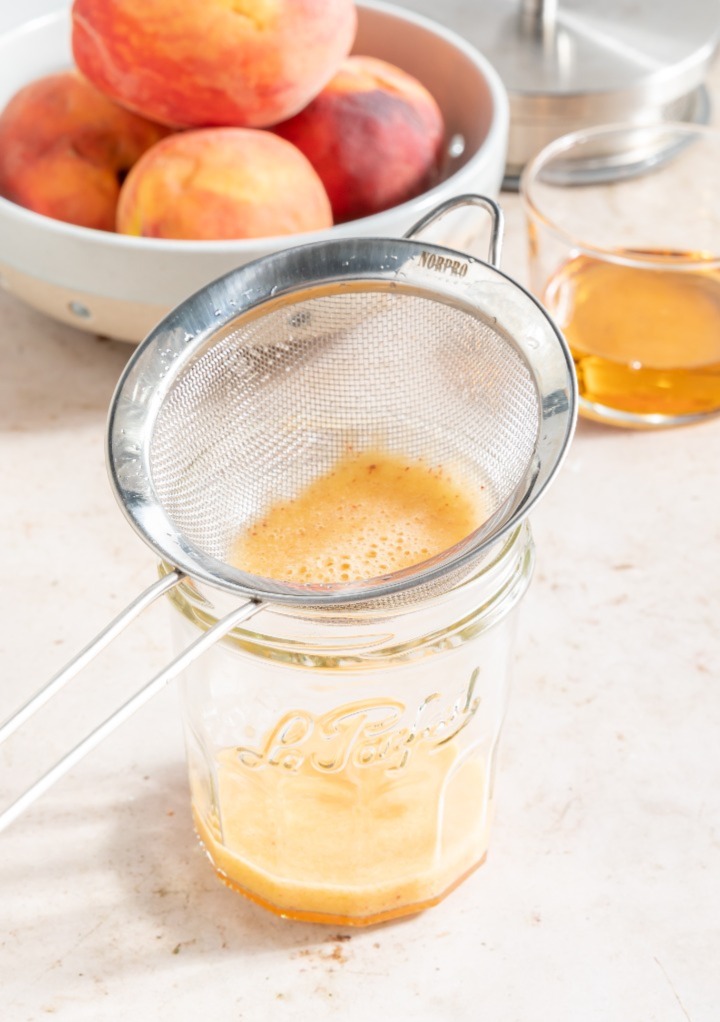 Peach puree with a small sieve straining over a glass.