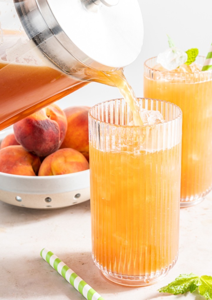 Pouring homemade peach tea in a clear glass with ice. 