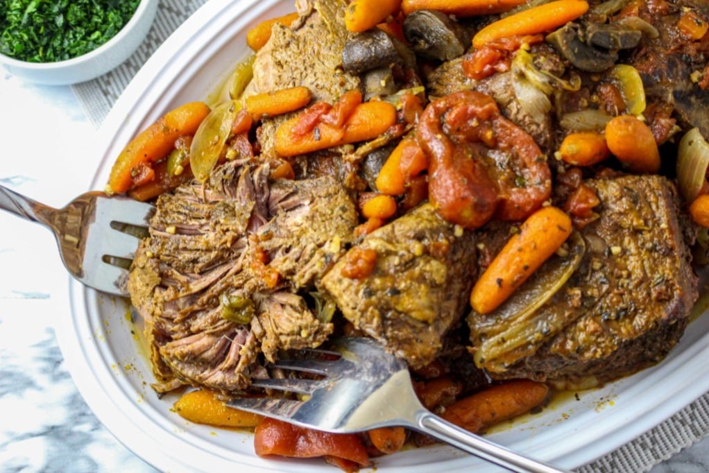 Cooked beef on a white serving dish pulled apart with two forks. 