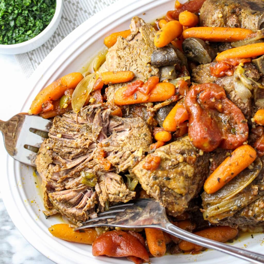 Fork tender pot roast on a white serving platter with carrots.