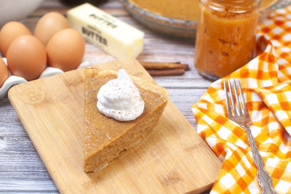 A slice of sweet potato pie with eggs in the background ready to eat. 