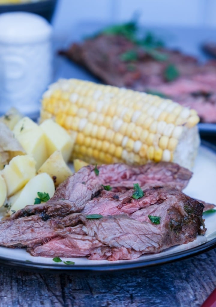 Broiled flank steak on a dinner plate with corn on the cob. 