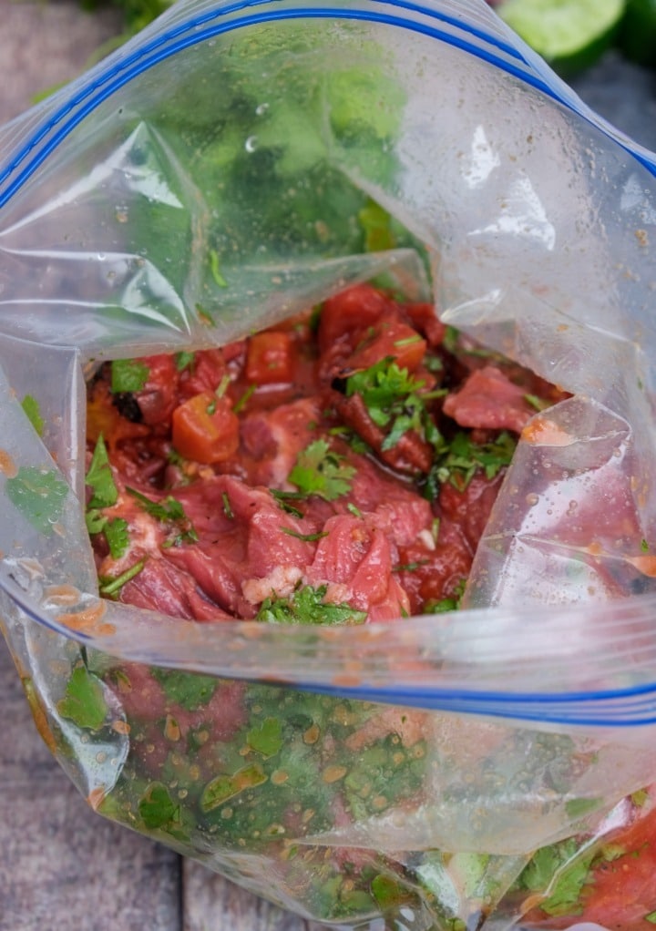 Cilantro and diced tomatoes added to steak in a ziplock baggie.