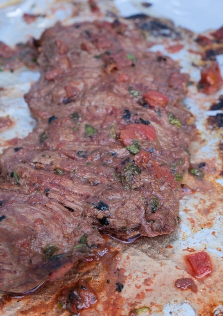 Broiled flank steak on a foil lined baking sheet. 
