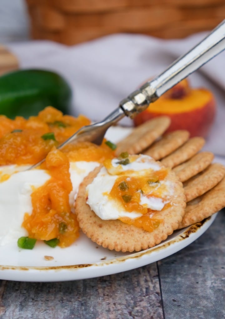 Ritz crackers with cream cheese and peach jam on a white serving plate. 