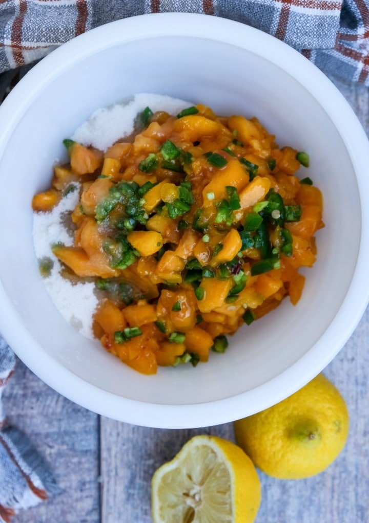 Diced peaches and jalapenos in a white mixing bowl. 