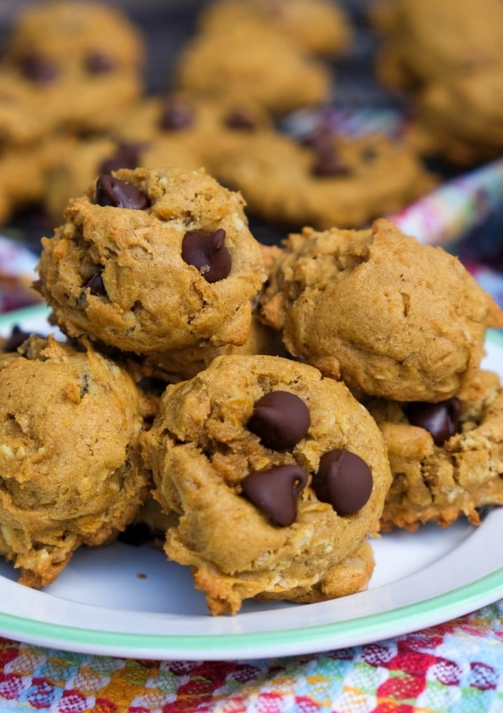 A pile of pumpkin oatmeal cookies with chocolate chips on a white plate. 