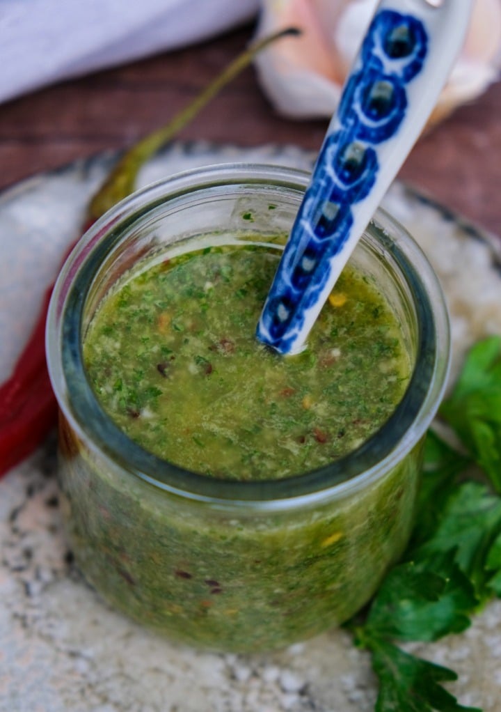 Fresh green spicy sauce to add to protein or vegetables with a small spoon in the center of the jar.  
