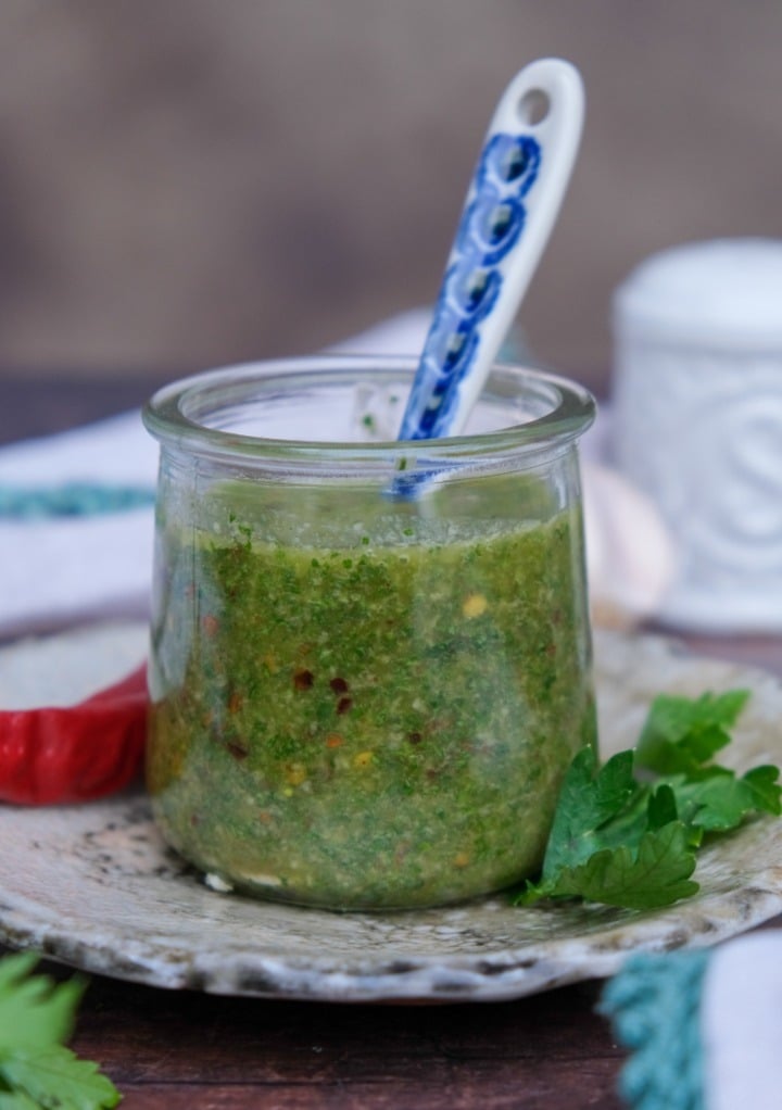 Spicy chimichurri sauce in a small clear jar with a serving spoon. 