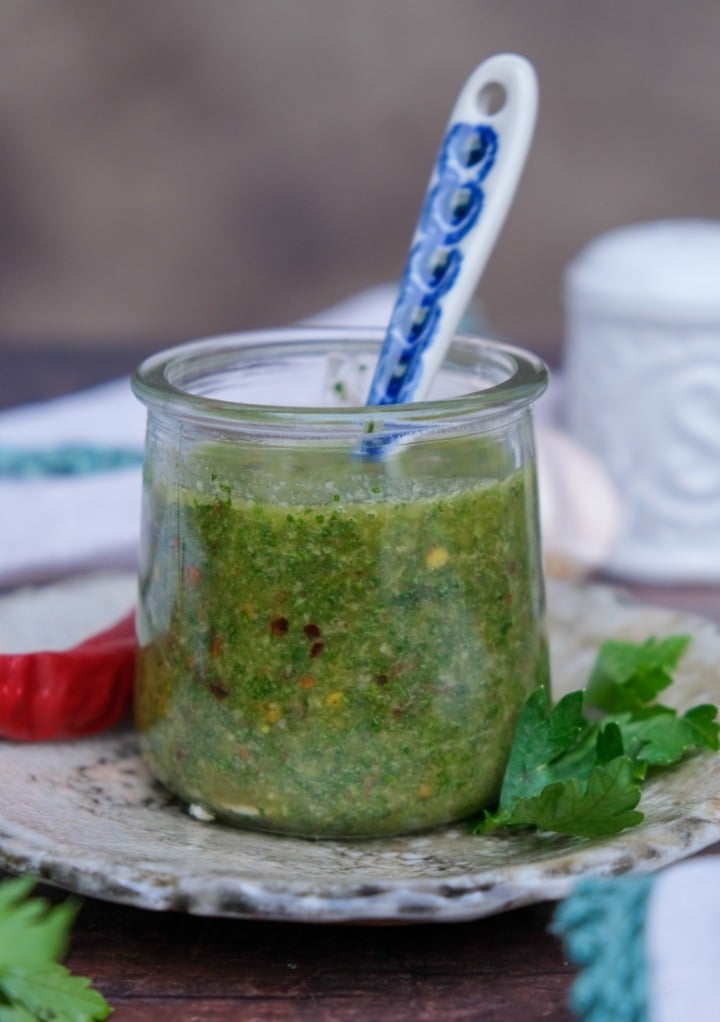 Spicy chimichurri sauce in a small clear jar with a serving spoon. 