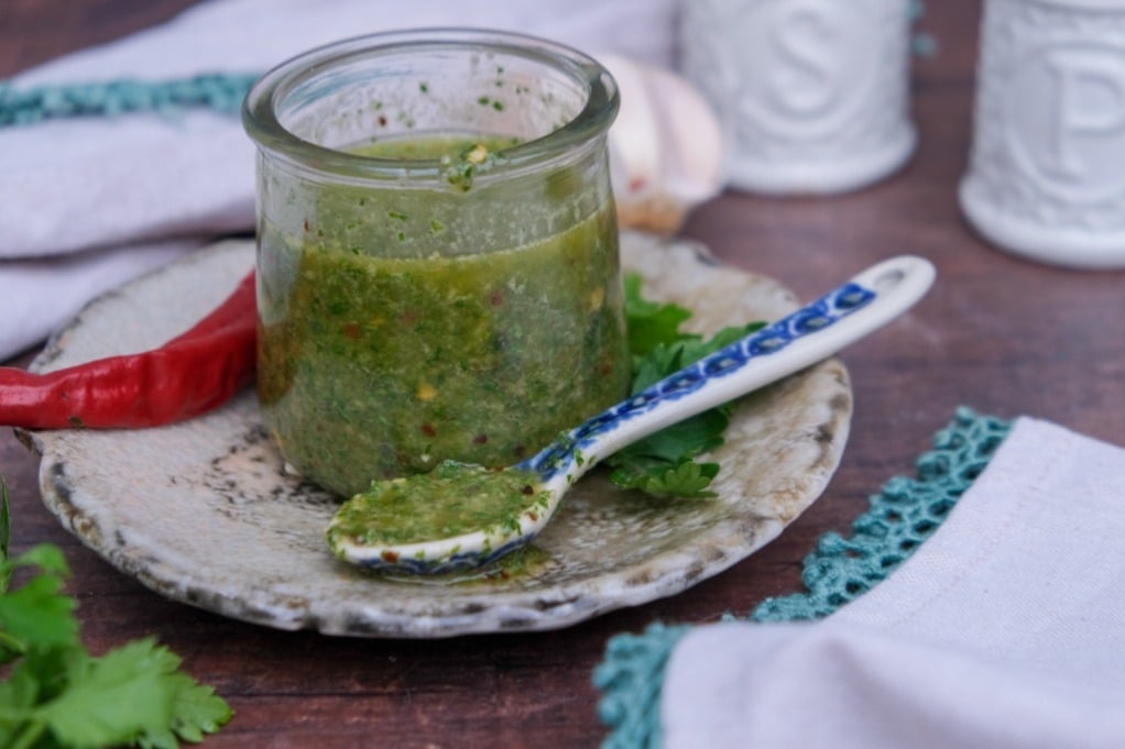 Easy homemade spicy chimichurri sauce recipe blended with peppers and herbs in a clear small jar. 