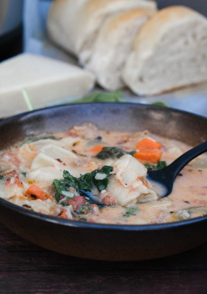 Instant Pot tortellini soup in a bowl with sliced bread on the side. 