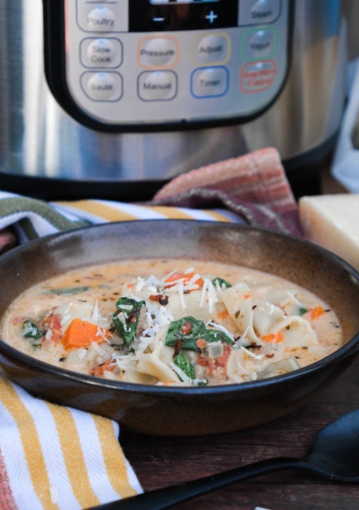 Tortellini soup in a brown bowl with an Instant Pot in the background. 