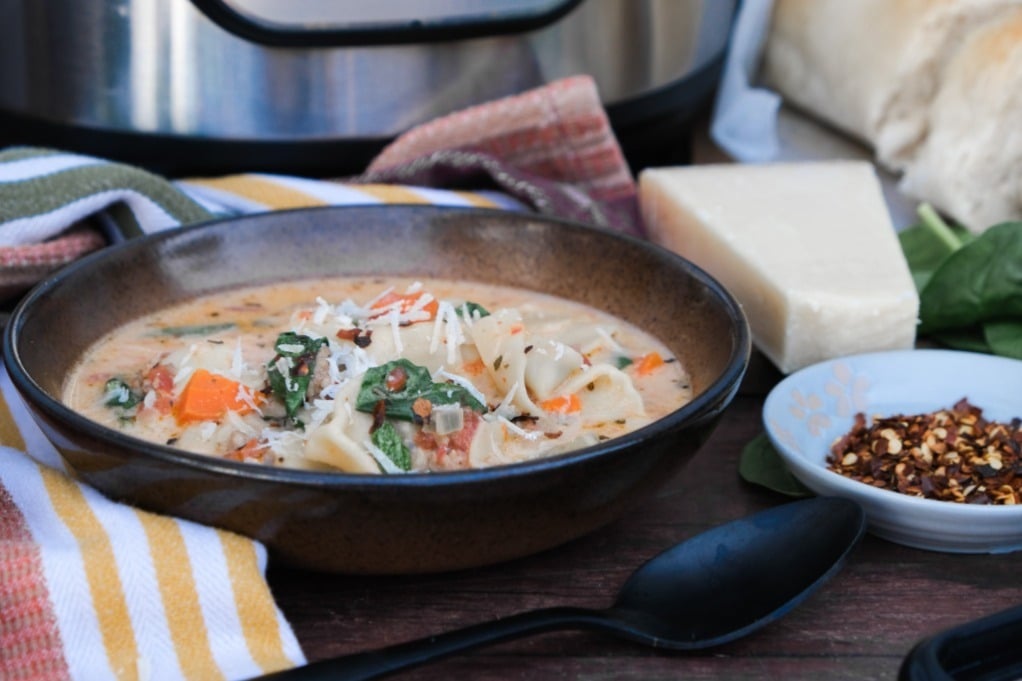 Creamy tortellini soup made in an Instant pot with red pepper flakes on the side. 