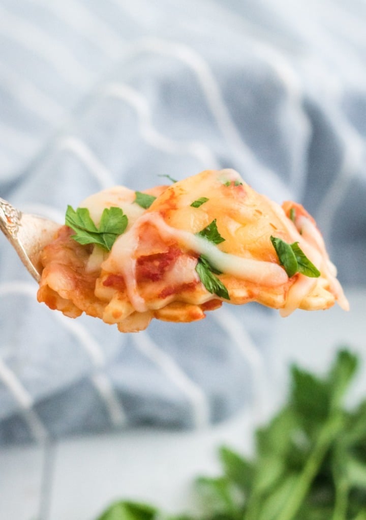 Forkful of lasagna topped with chopped parsley.