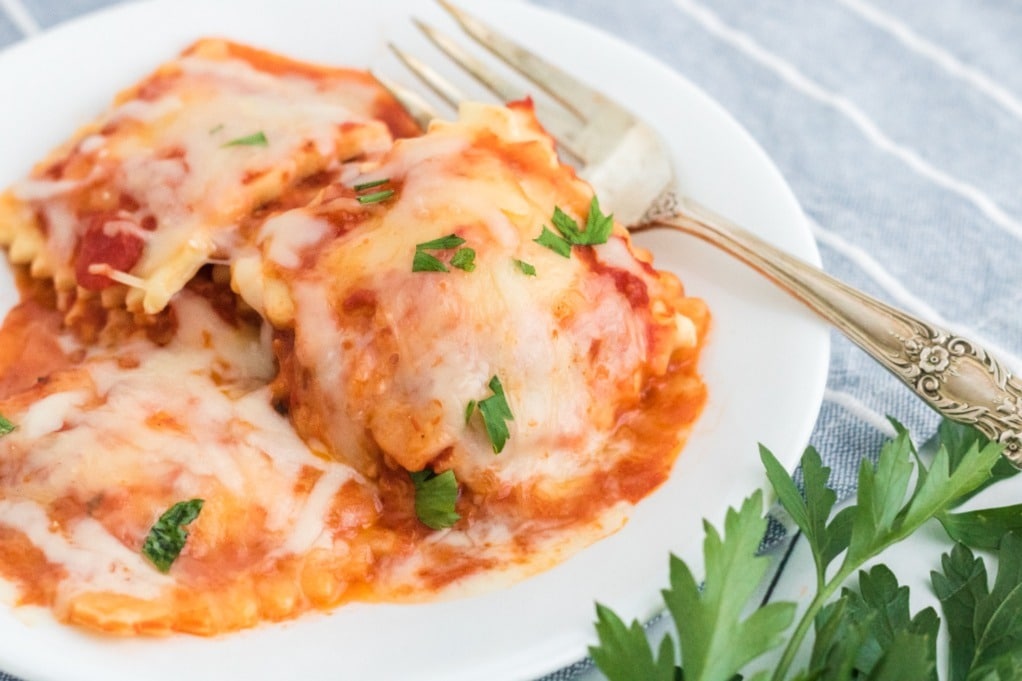 Lasagna made with ravioli on a white plate with a fork on the side. 