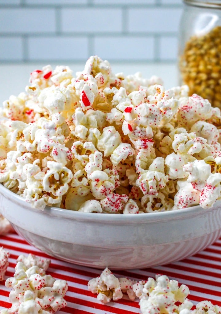A white bowl with white chocolate popcorn with peppermint candy.