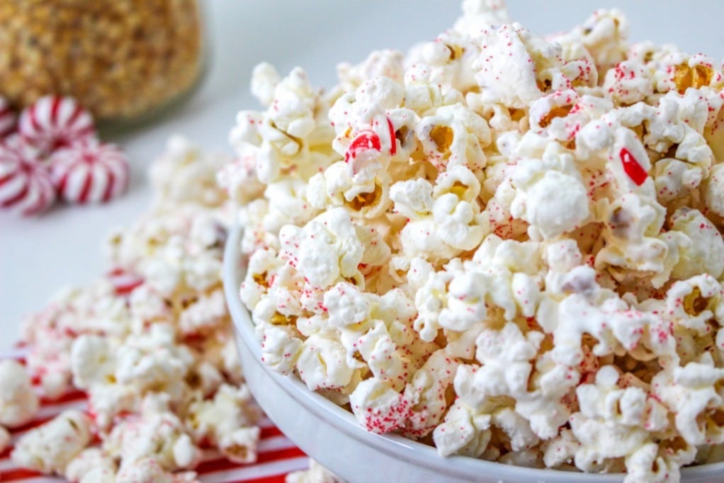 White chocolate popcorn coated with peppermint candy in a white bowl. 