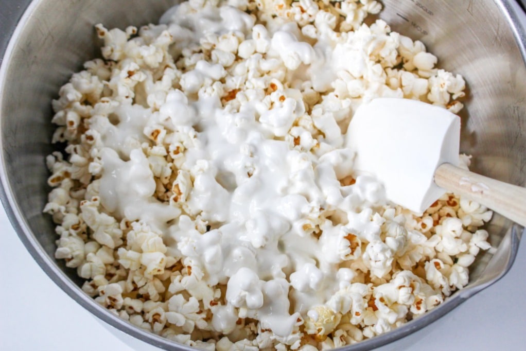 Melted white chocolate poured over fresh popcorn in a mixing bowl.