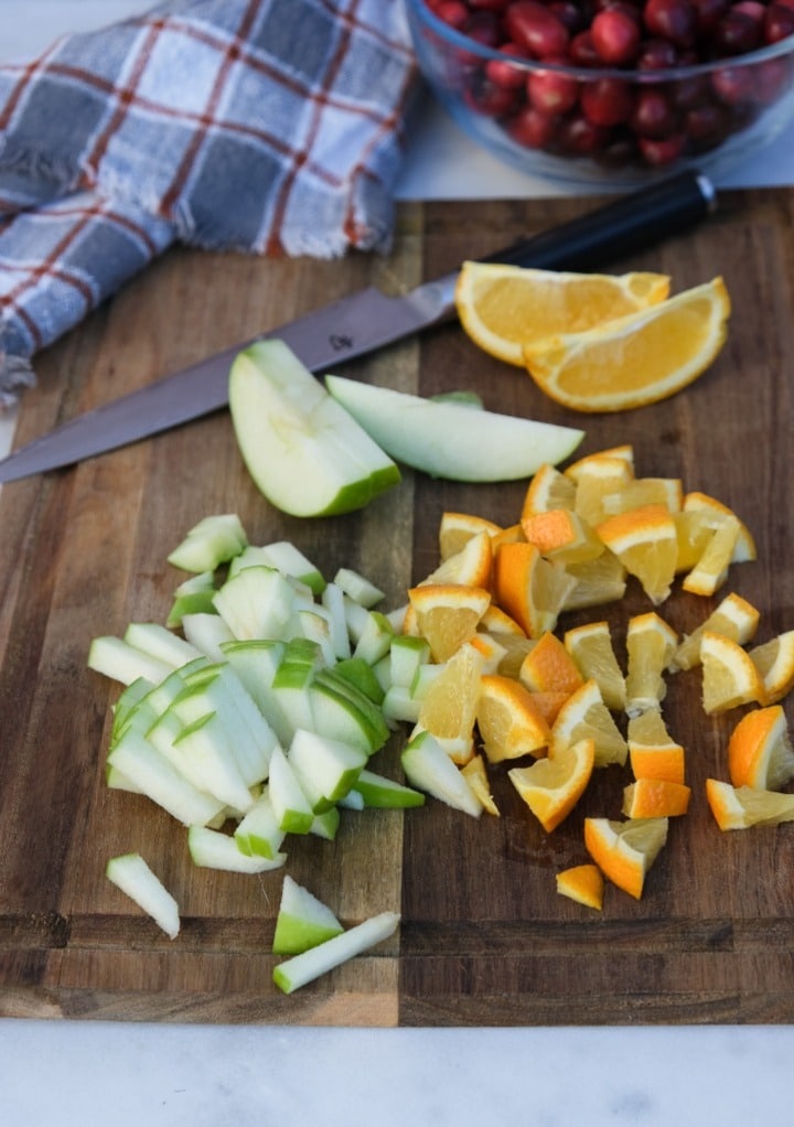 Diced green apple and a whole orange on a brown cutting board. 