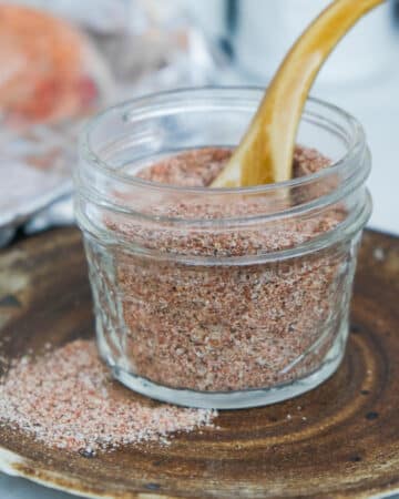 A mix of spices in a small mason jar on a brown plate.