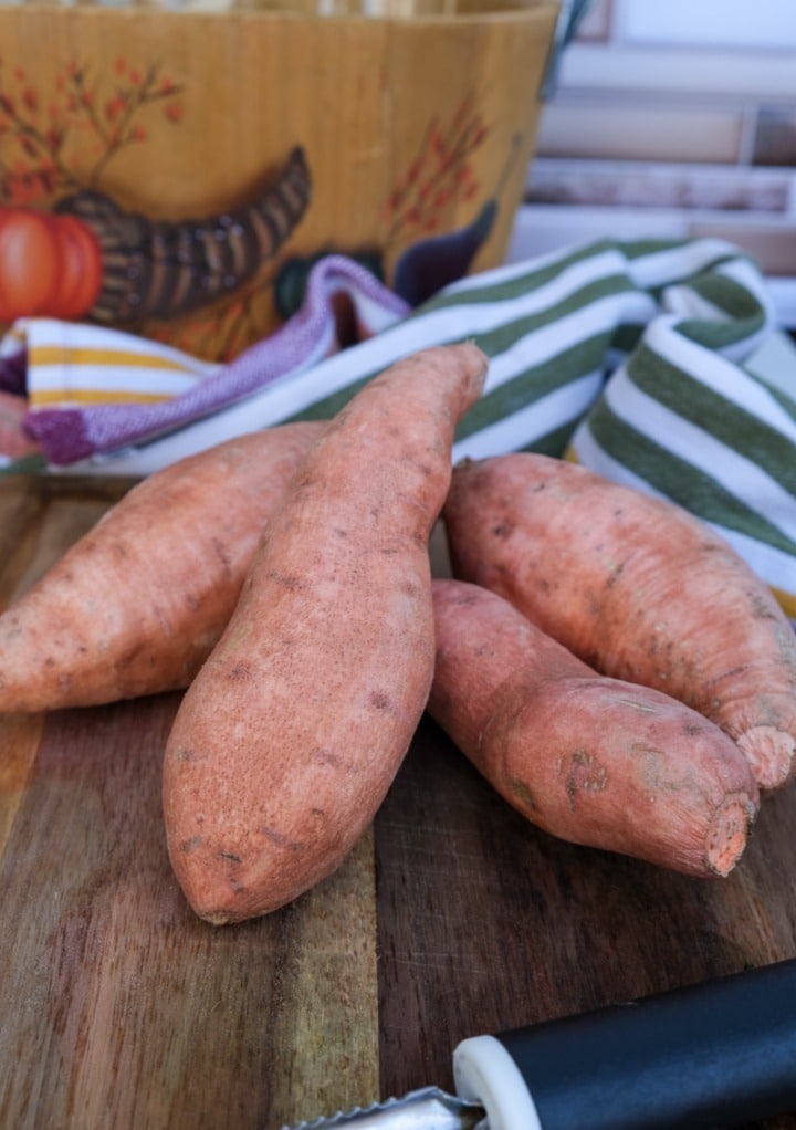 Fresh sweet potatoes on a brown cutting board. 