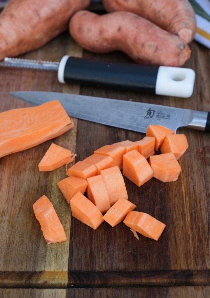 Dicing sweet potatoes on a brown cutting board. 