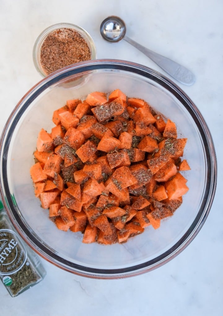 A clear bowl with diced sweet potatoes topped with spices. 