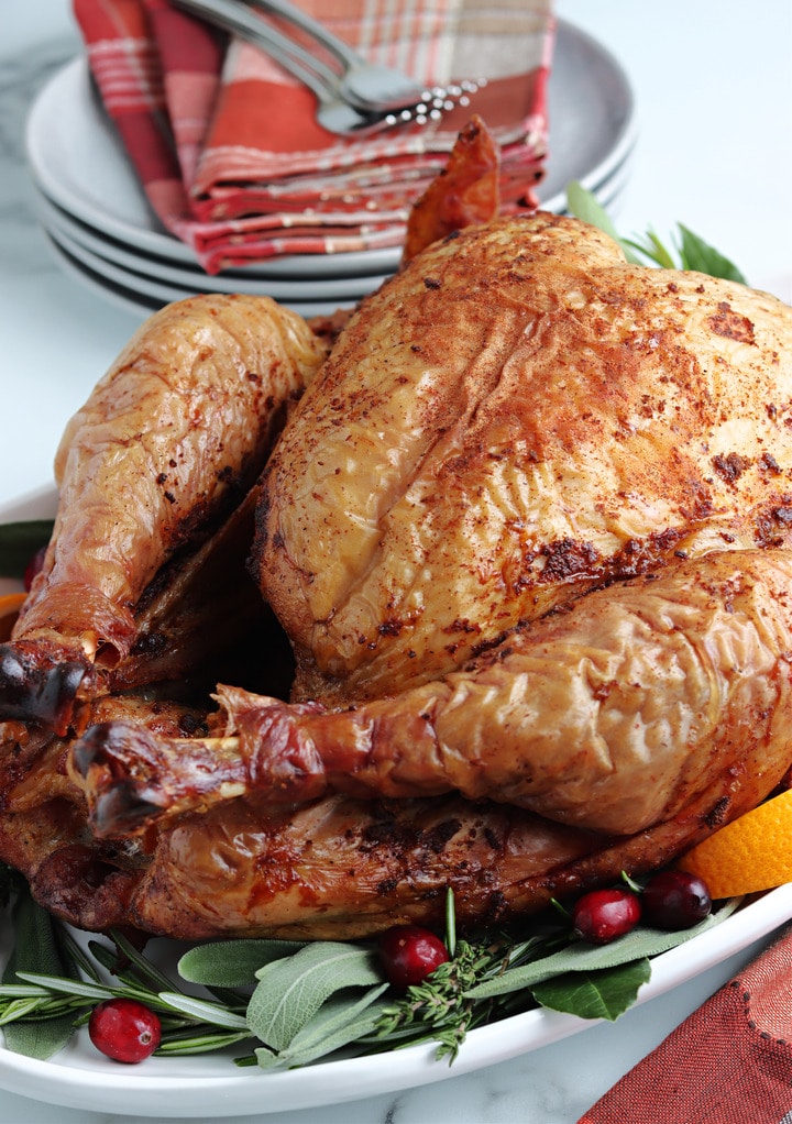 Cooked smoked turkey on a white serving platter with cranberries. 