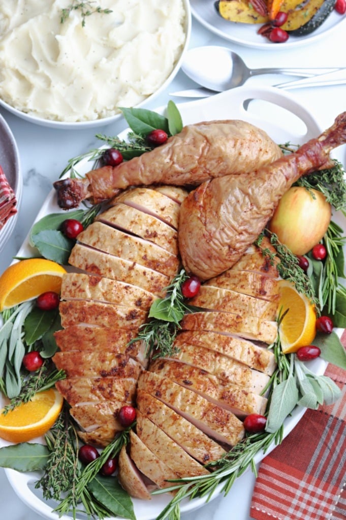 Smoked turkey sliced and placed on a serving dish with sliced oranges, greens and cranberries. 