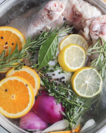 Top view of fruits and herbs with a whole turkey in a brine mixture.
