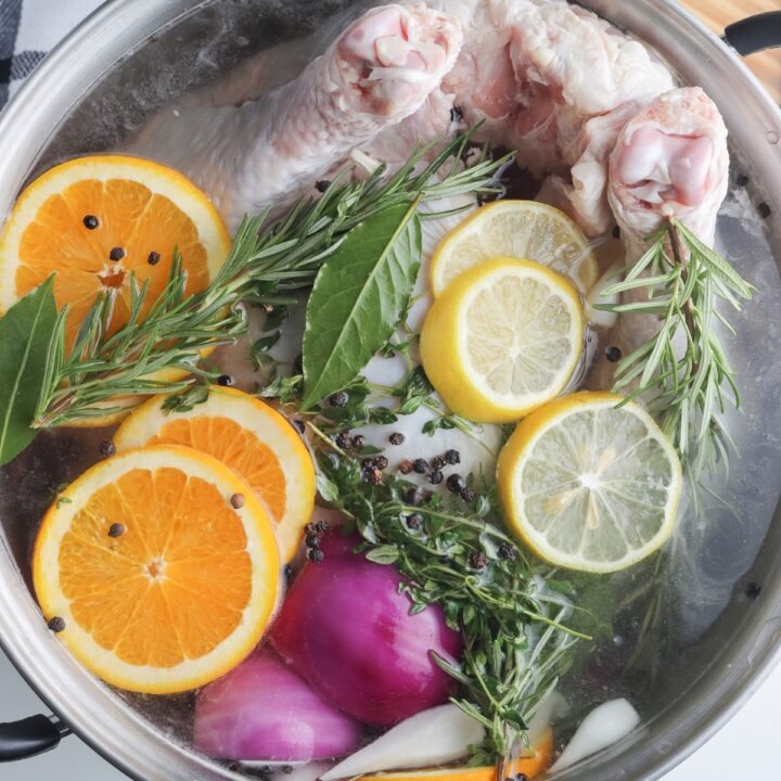 Top view of fruits and herbs with a whole turkey in a brine mixture.