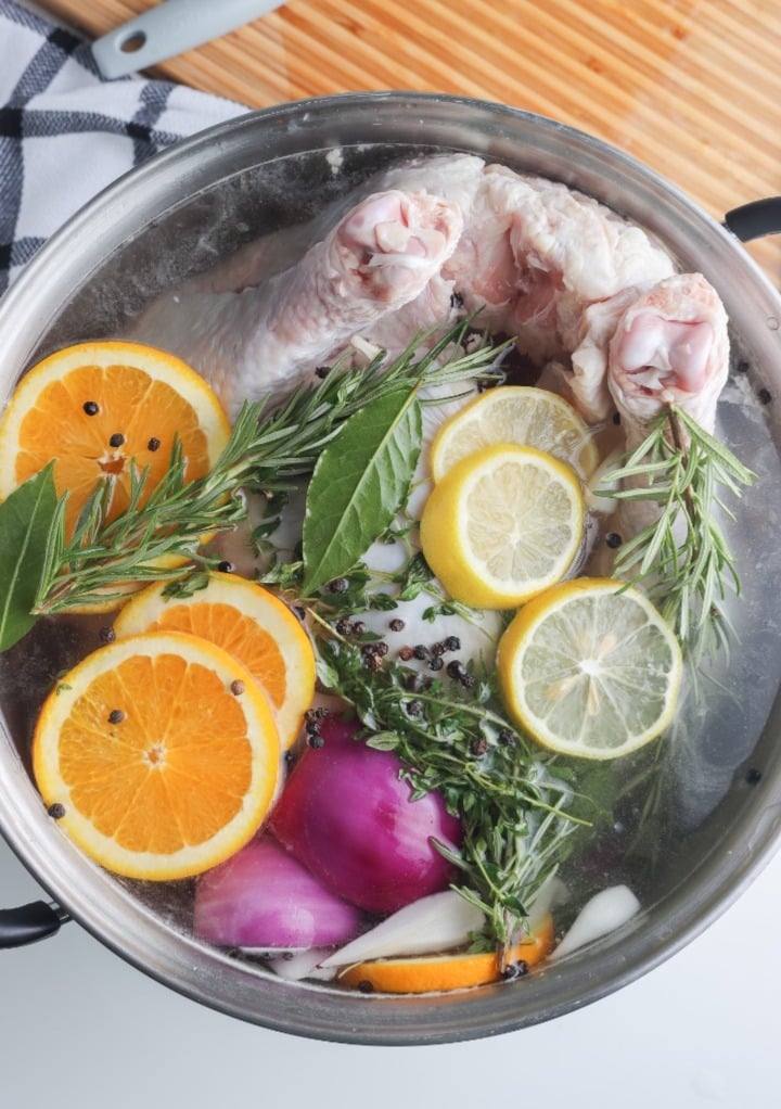 A whole turkey in a large stockpot with a brining mixture with sliced oranges and lemon. 