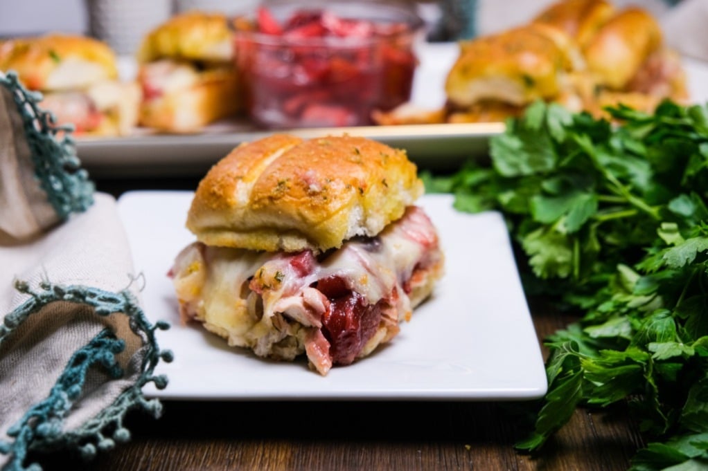 Baked turkey slider on a white plate the more sandwiches in the background. 