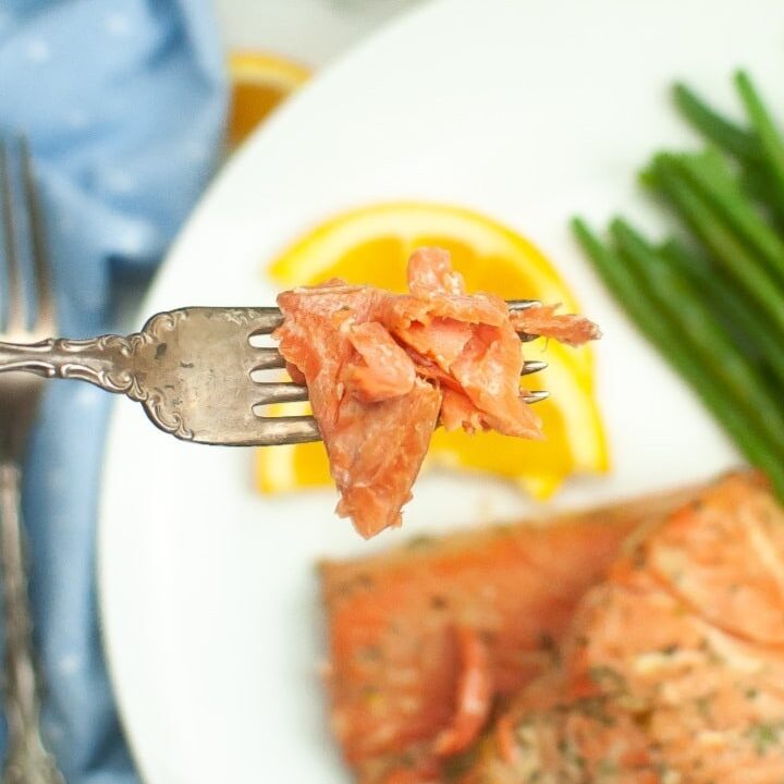 A forkful of flaky salmon over a dinner plate.