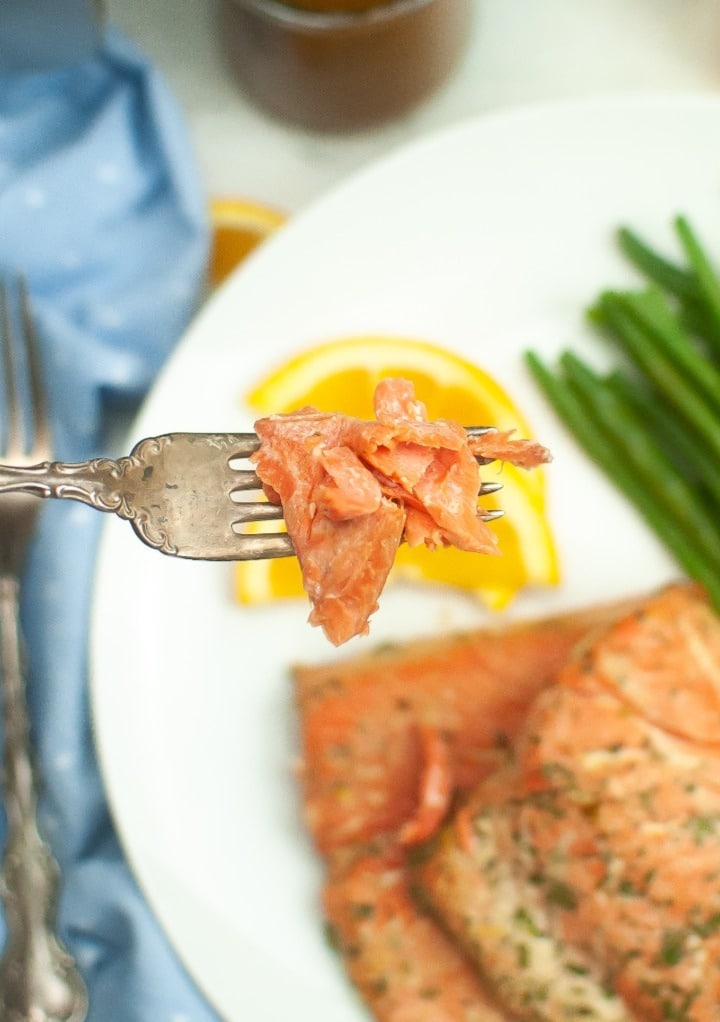 A forkful of flaky salmon over a dinner plate. 