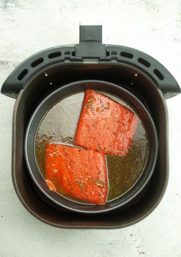 Fresh salmon fillets placed in a baking pan and placed in the air fryer basket ready to cook.